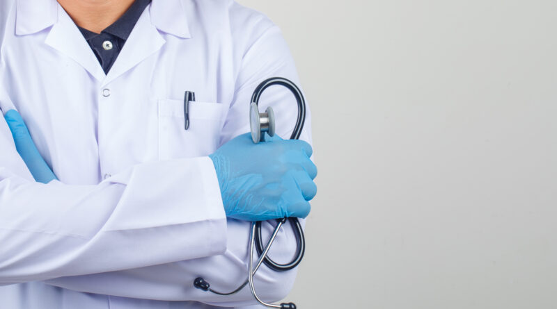 Doctor crossing arms while holding stethoscope in white coat front view.